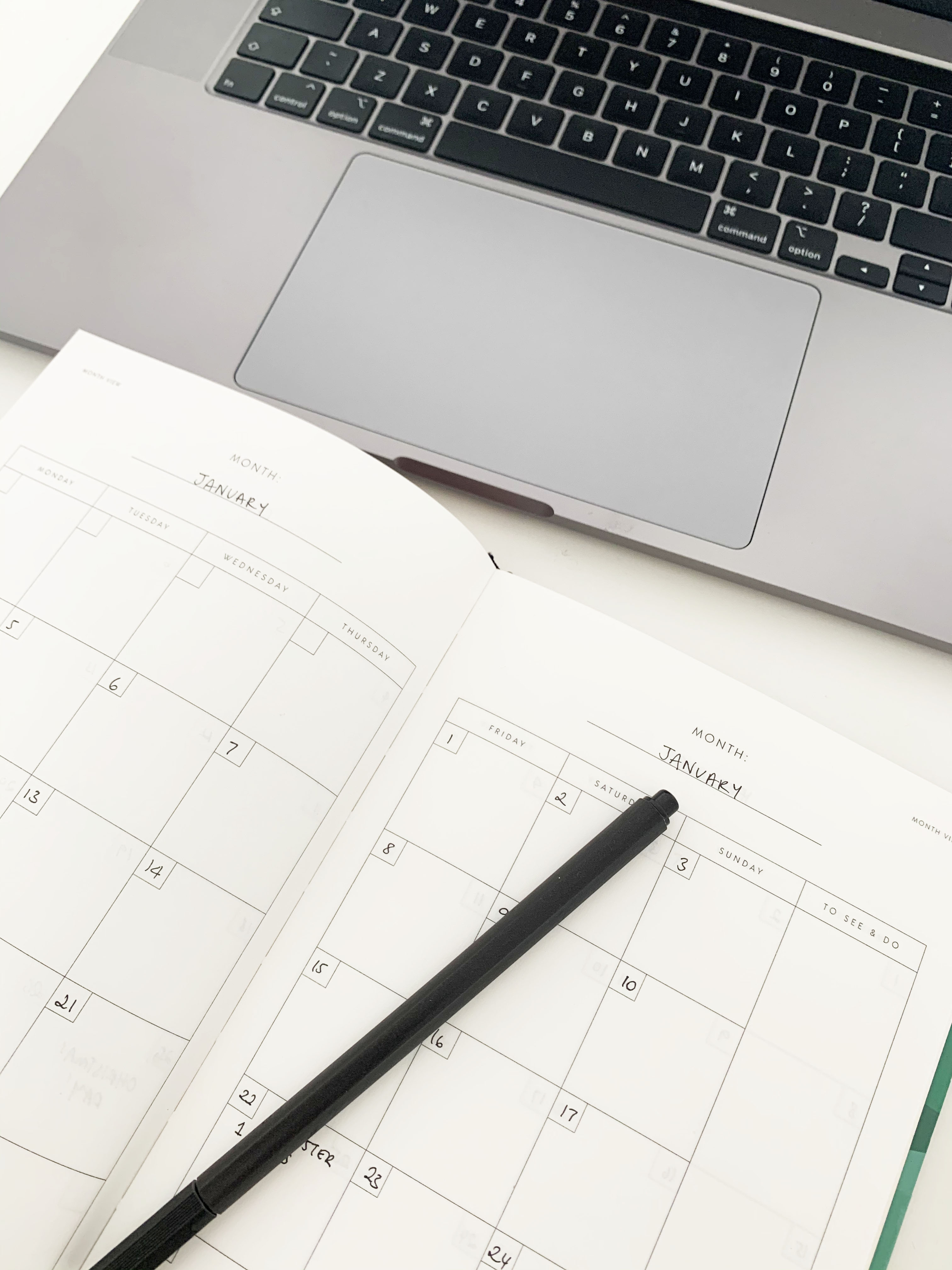 Image shows a laptop and an open diary sitting on a desk