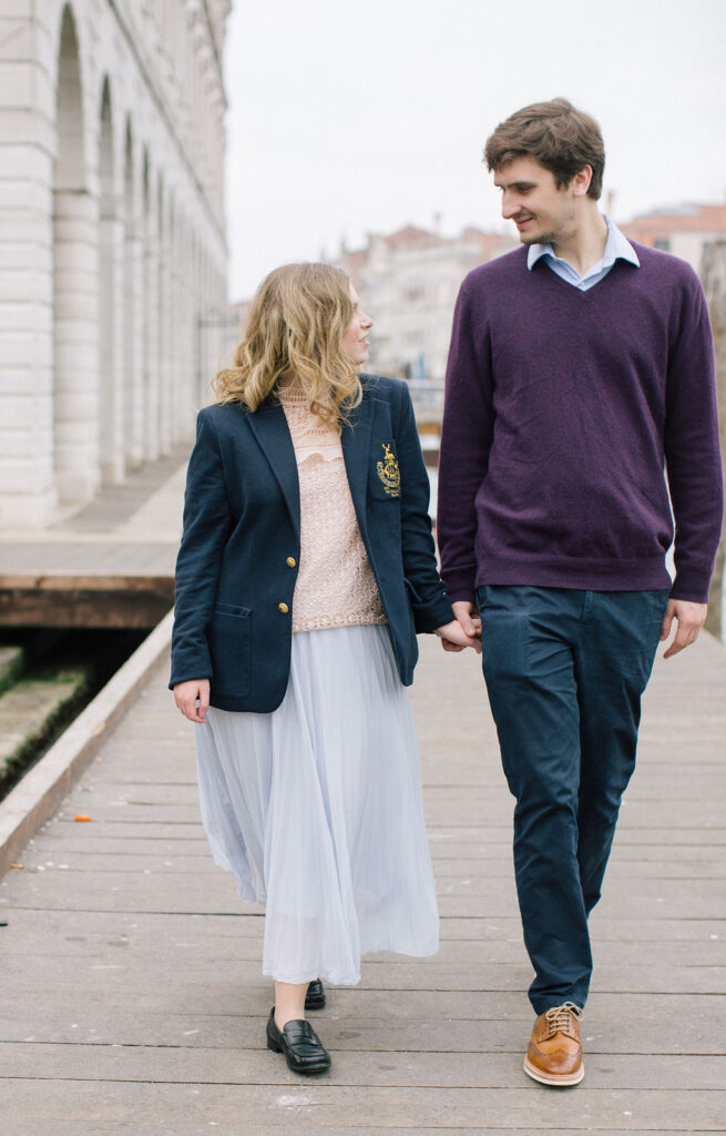 Photo of Sophie looking at Ryan in Venice near the Grand Canal. Sophie is wearing a navy Ralph Lauren blazer with pale pink Zara top and a pleated pale blue skirt and loafers. Ryan is wearing a plum coloured cashmere jumper and Ralph Lauren navy chinos 